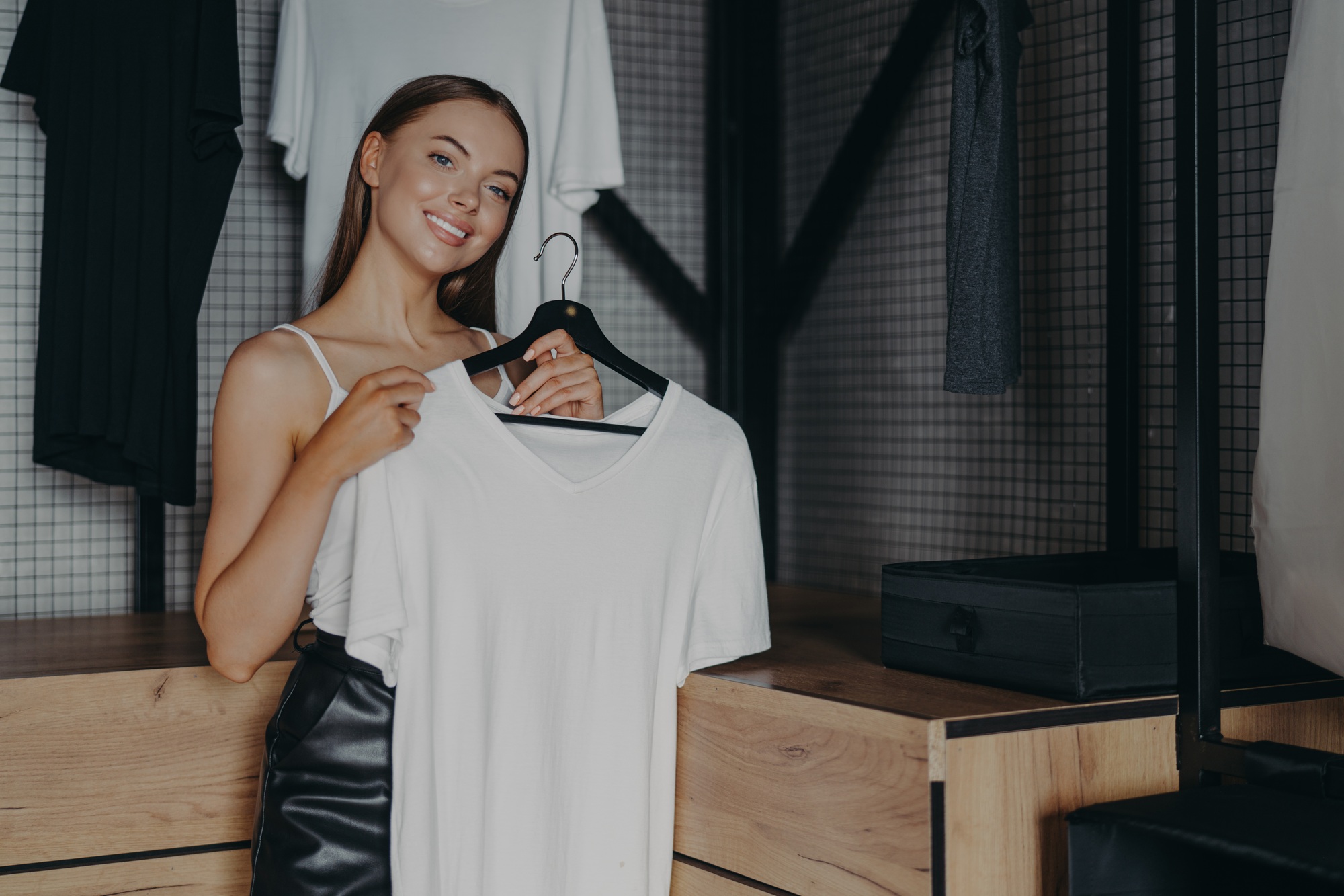 Positive woman dresses for special occasion, holds white dress on hangers, poses over home wardrobe