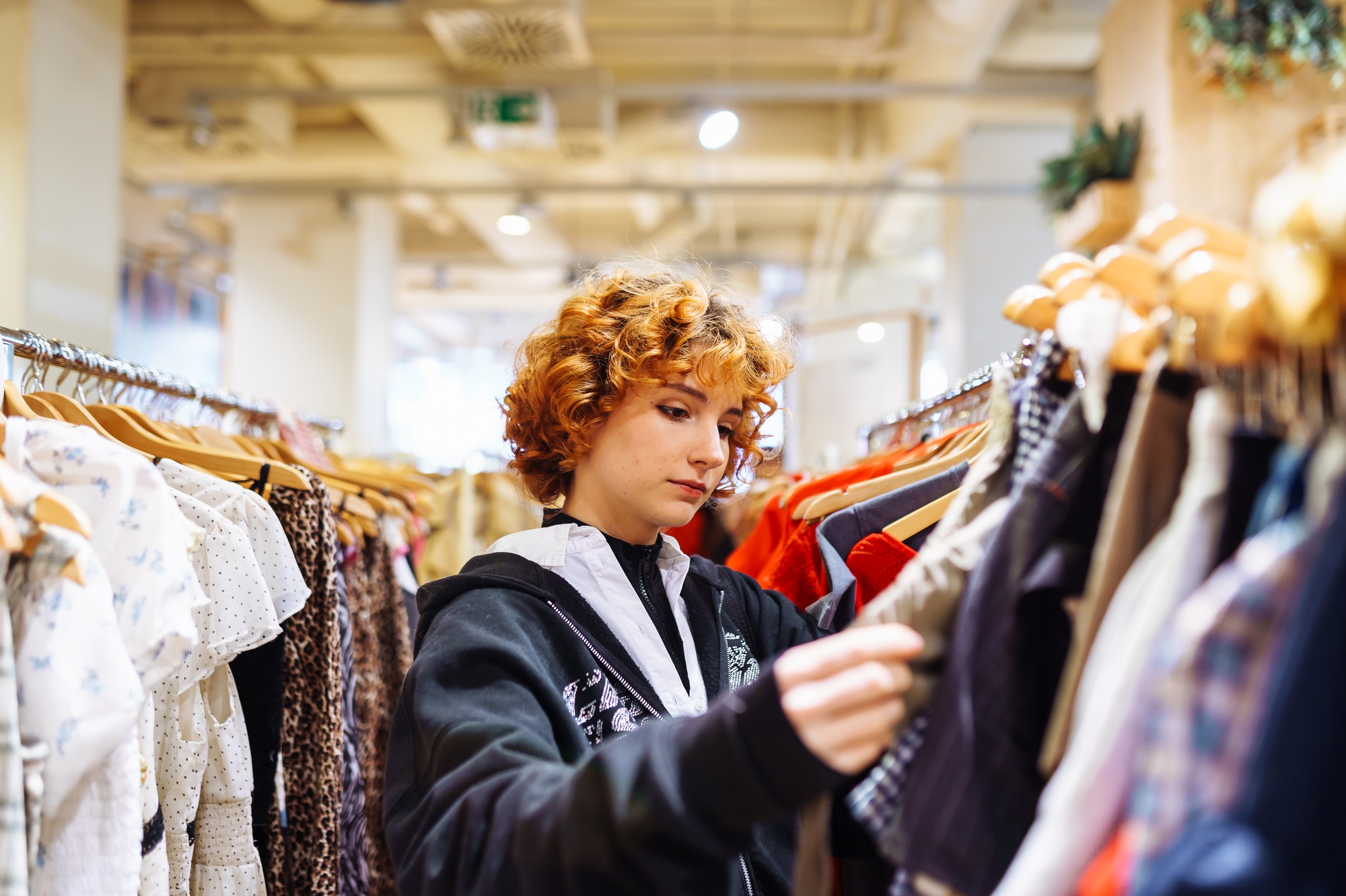 portrait of red-haired attractive young woman trying on clothes in store
