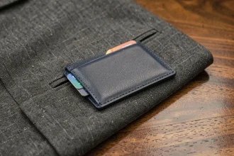 Porte carte fin en cuir bleu marine posé sur la poche d'un costume en laine gris anthracite, vue en gros plan mettant en valeur son épaisseur réduite